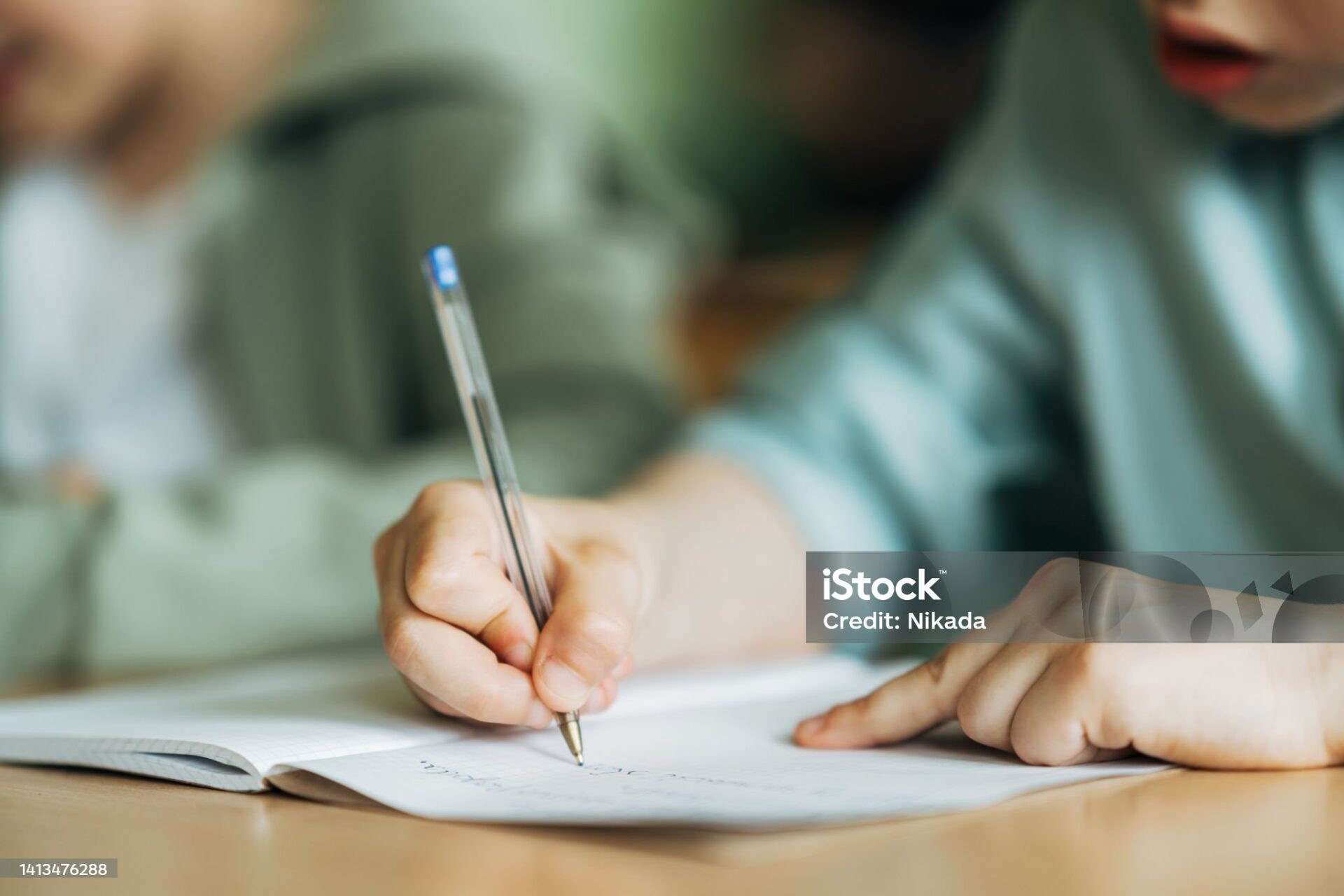 Close-up of a  boy writing with a pen in workbook. Elementary schoolboy sitting on desk and studying in classroom.